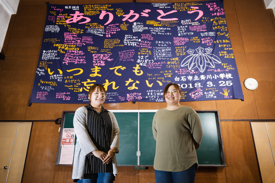 お二人は斎川地区で生まれ育ち、幼稚園から中学校まで一緒の学校で学びました。（閉校を迎えた斎川小学校の平成30年度卒業生の寄せ書きの前にて）